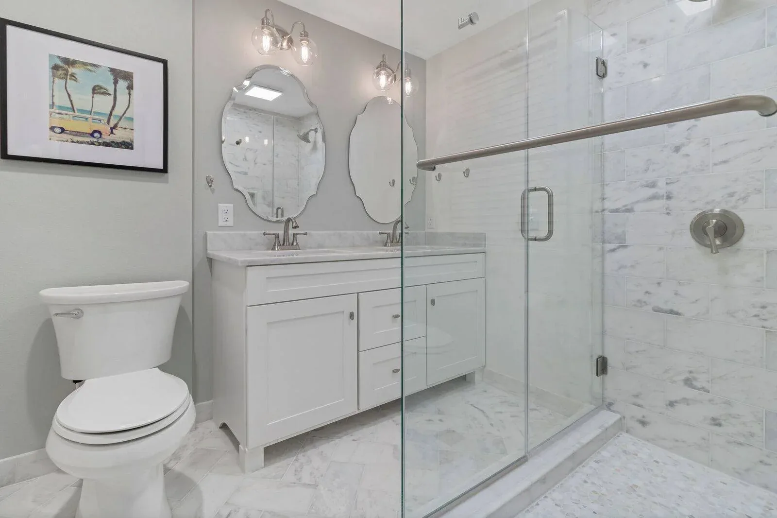 Remodeled bathroom with a double vanity, framed mirrors and a glass shower